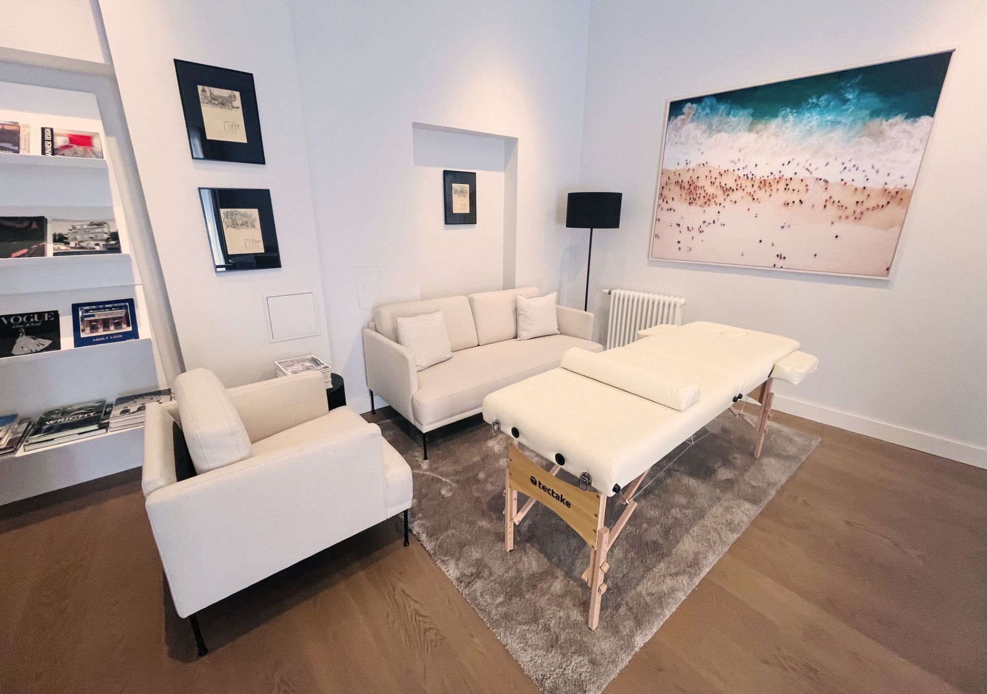 Ein Bild von einer Behandlungsliege, sowie 2 Sofas in einem weißen Raum mit Bildern an der Wand
